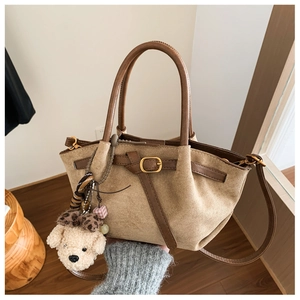 Detailed shot of khaki suede handbag featuring brown leather handles and a plush bear charm