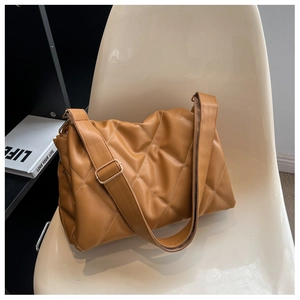 Detail der karamellfarbenen Stepptasche mit breitem Gurt und goldener Hardware am Stuhl
