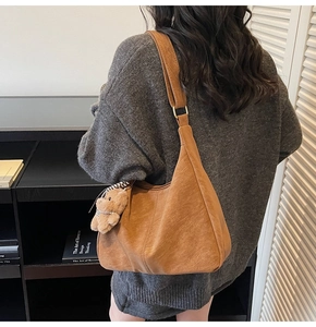Dettaglio della grande borsa hobo in pelle marrone con texture vintage e charm a orsetto