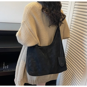 Detail of a large black matte crescent tote bag worn by a model in a knit sweater