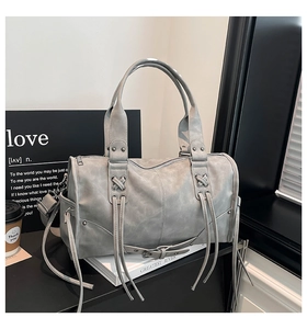 Detail view of the gray distressed tote bag with long tassels and woven decoration