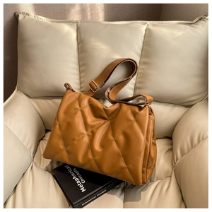 Detail der karamellfarbenen Stepptasche mit breitem Gurt auf cremefarbenem Sofa