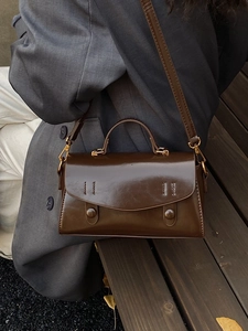Deep brown vintage leather handbag with gold metal hardware on grey suit model