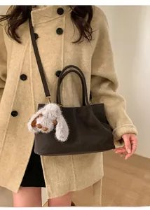 Détail d'un sac cabas en daim marron foncé avec breloque lapin et bandoulière