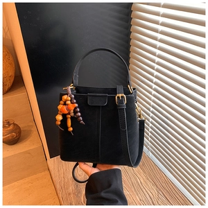 Detail of a black bucket bag with a wooden bead charm and adjustable strap on a wood table