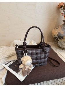 Detail of vintage plaid bucket bag featuring a plush bear charm and leather strap