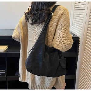 Detail of black leather tote bag with wide strap and matching round charm worn over a sweater