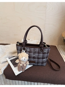 Detail of retro plaid bucket bag with brown leather handles and plush bear charm