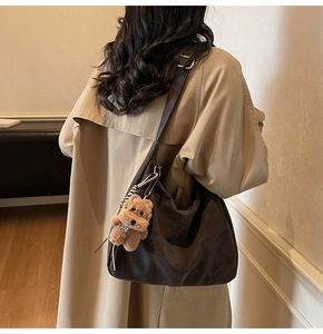 Dettaglio borsa hobo in pelle testa di moro con ciondolo a orsetto e trench beige