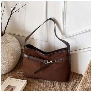 Detailed view of dark brown suede shoulder bag with gold buckles in vintage room setting