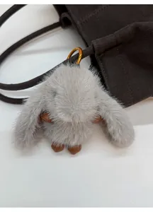 Close-up of a grey plush rabbit charm with a gold hook on a brown suede bucket bag