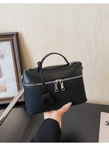 Detail of black leather handbag featuring dual silver zippers and a minimalist square pendant