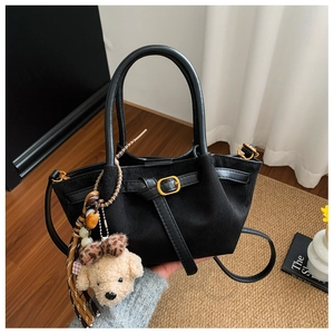 Detail of black suede bucket bag featuring metallic buckle, beads, and plush puppy charm