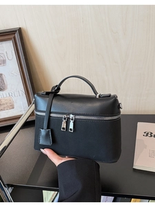 Close-up of a matte black handbag featuring dual silver zippers and a top curved handle