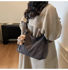 Dettaglio borsa hobo grigio scuro con ciondolo a forma di cucciolo su modella in interni