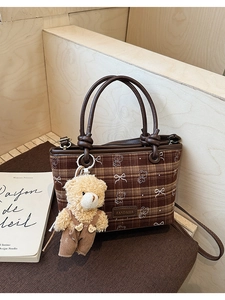 Detail of brown plaid bucket bag featuring a bear charm and leather handles