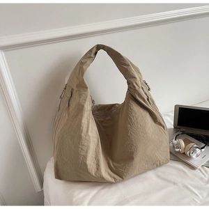 Large khaki pleated tote bag with drawstring detail next to a laptop and headphones