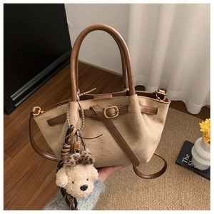 Detail of khaki suede handbag with brown leather straps and a cute teddy bear charm