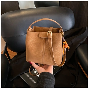Detail of a brown lychee pattern leather bucket bag with decorative beaded keychain
