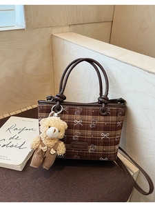 Detail of brown plaid bucket bag featuring a bear plush pendant and chic logo print