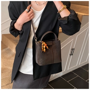 Détail du sac seau en daim marron foncé avec pompon chic en perles de bois et bandoulière