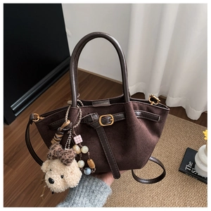 Detail of dark brown suede tote bag featuring a leather buckle strap and plush bear charm