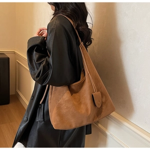 Brown suede tote bag side view with decorative tassel charm shown on a model coat