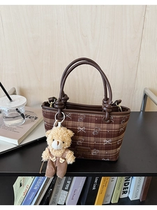 Detail of a brown plaid bucket bag featuring bow bear patterns and a plush bear pendant