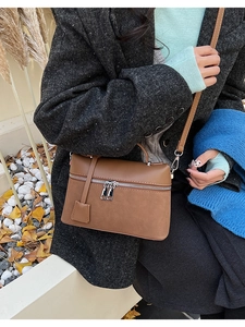 Detail of a brown matte leather shoulder bag with silver dual zipper and square charm