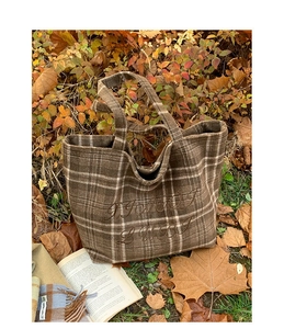 Close-up of brown plaid wool tote bag with floral embroidery on autumn leaf background