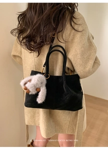 Detail of a vintage black suede bucket bag with long strap and plush bunny charm accessory