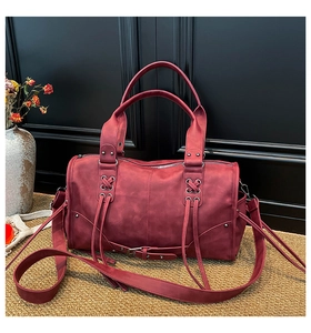 Detail of burgundy leather Boston bag featuring moto-style rivets and buckle accents