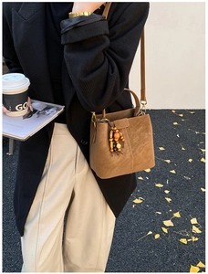 Brown suede bucket bag with wooden beads detail held by model on autumn leaf street
