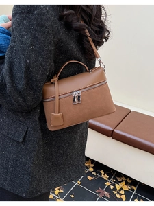Detail of a brown leather crossbody camera bag with dual zippers and top handle outdoors