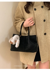 Close-up of a black suede tote bag with a white plush rabbit pendant on a wool coat