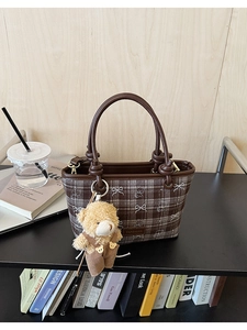 Detailed view of a brown plaid bucket bag featuring cartoon bear motifs and a plush charm