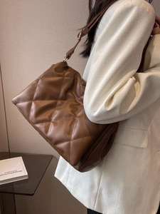 Braune gesteppte Schultertasche mit breitem Riemen am Model im weißen Blazer gezeigt