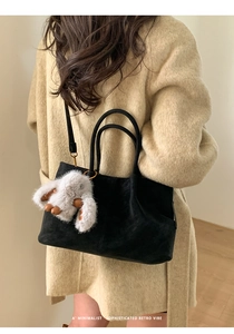 Close-up of black suede tote bag with plush rabbit charm on beige coat model