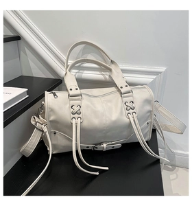 Detail of cream biker bag with decorative tassels, silver studs, and lace-up details