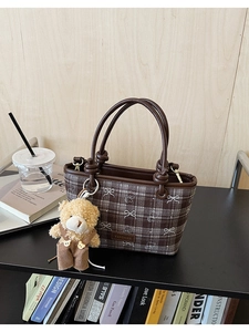 Detail of coffee plaid bucket bag featuring a plush bear charm and leather handles