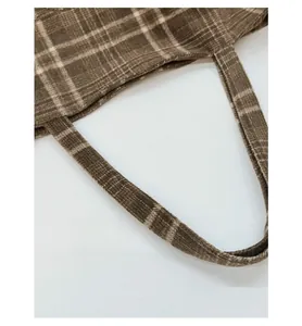 Detail of the widened shoulder strap on a brown plaid wool tote bag for comfort