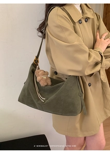 Détail d'un sac hobo vert foncé avec pendentif ours sur trench-coat kaki