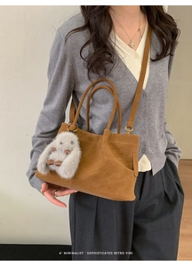 Detail of a brown suede tote bag featuring a cute grey plush rabbit pendant accessory