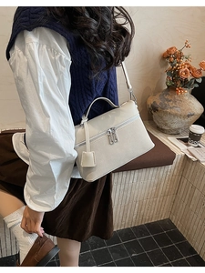 Detailed side view of a white textured leather crossbody bag with a single handle and tag