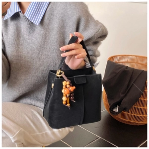Close-up of black bucket bag featuring unique wooden beaded charm and gold hardware