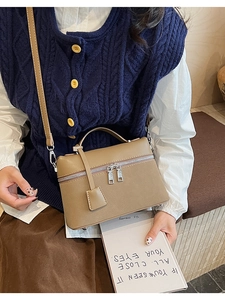 Close-up of khaki satchel bag with dual zippers and leather tag on a stylish model outfit