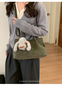 Deep green suede tote bag with grey bunny charm shown on a model in a minimalist setting
