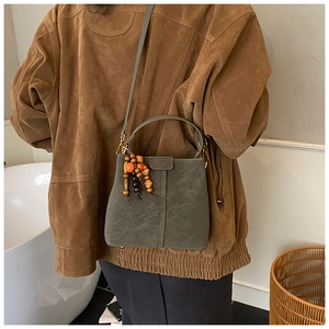 Detail of grey-green bucket bag with wooden bead tassels and adjustable shoulder strap