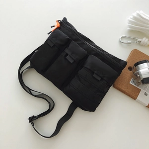 Détail du sac bandoulière tactique noir avec trois poches à rabat et cordons orange