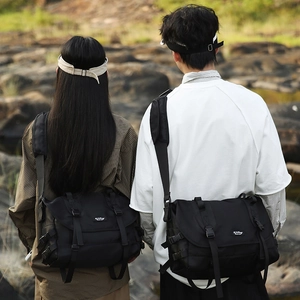 Outdoor shot of couple wearing black waterproof messenger bags showing unisex design and fit